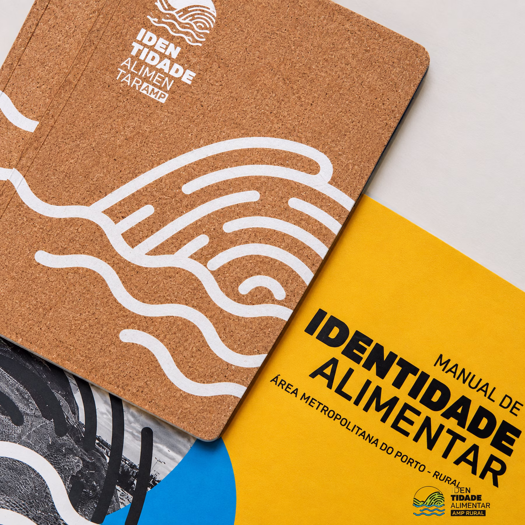 Cork notebook printed with the Identidade Alimentar mark, next to the yellow brand manual